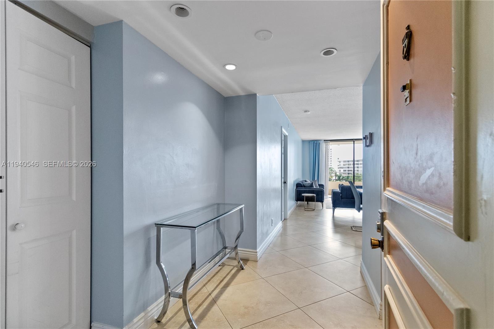 A light blue entryway leads to a living area with tile floors and a balcony — 600 Three Islands Blvd # 519, Hallandale Beach FL 33009, HALLANDALE BEACH, FL