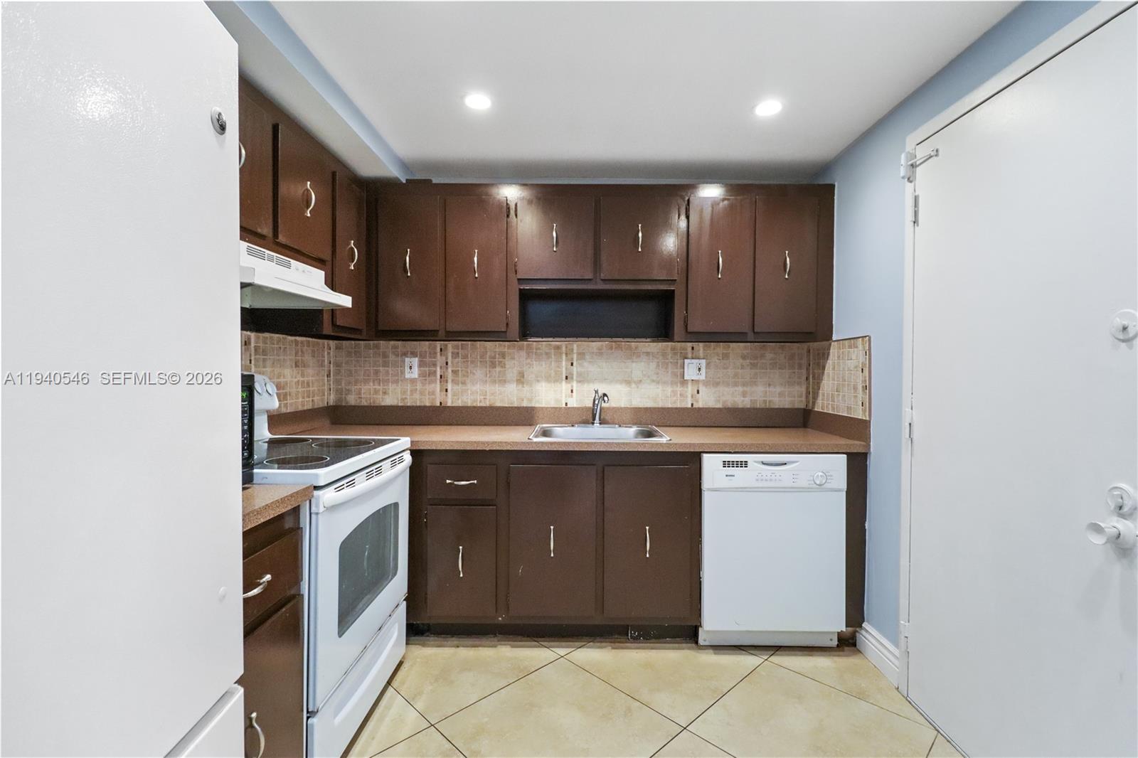 A kitchen features brown cabinets, a white stove, a white dishwasher, and tiled flooring — 600 Three Islands Blvd # 519, Hallandale Beach FL 33009, HALLANDALE BEACH, FL
