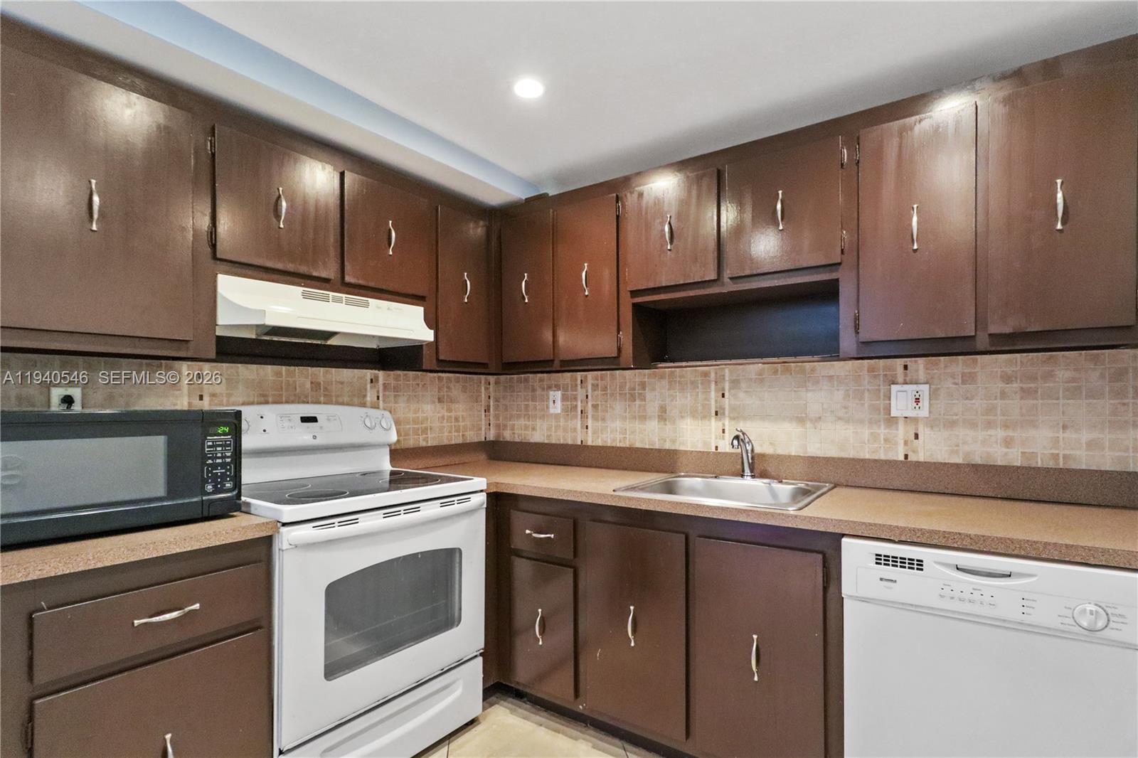 A kitchen features brown cabinets, a white stove, a white dishwasher, and tan countertops — 600 Three Islands Blvd # 519, Hallandale Beach FL 33009, HALLANDALE BEACH, FL