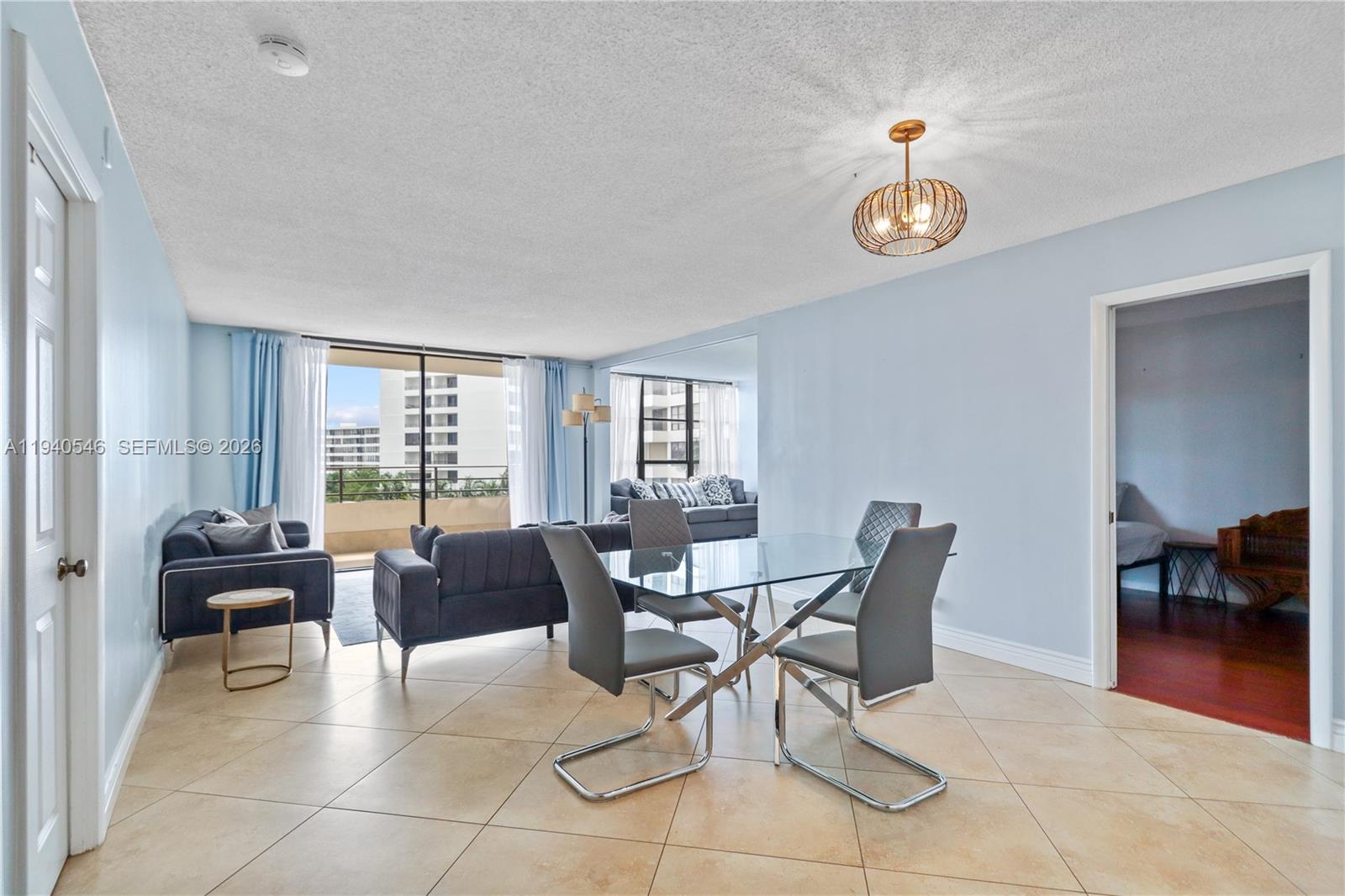 A dining area with a glass table and chairs sits adjacent to a living room — 600 Three Islands Blvd # 519, Hallandale Beach FL 33009, HALLANDALE BEACH, FL