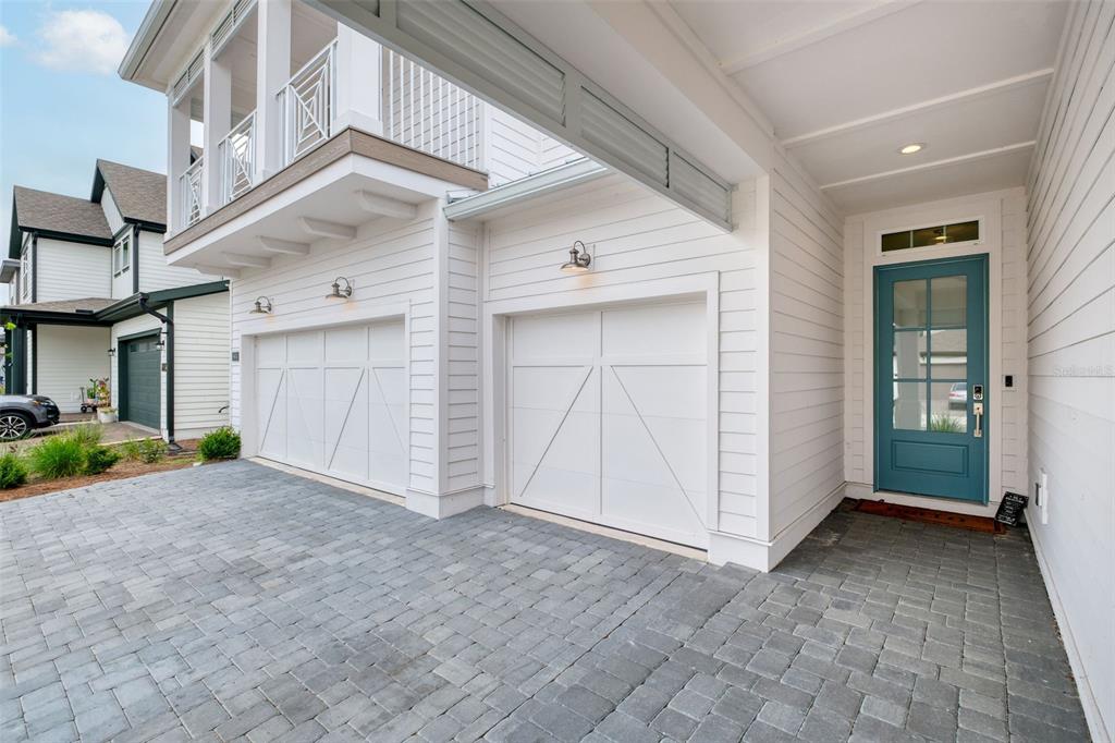A white house exterior features a two-car garage, a teal front door, and paver driveway — 6604 QUEST STREET, ST CLOUD, FL