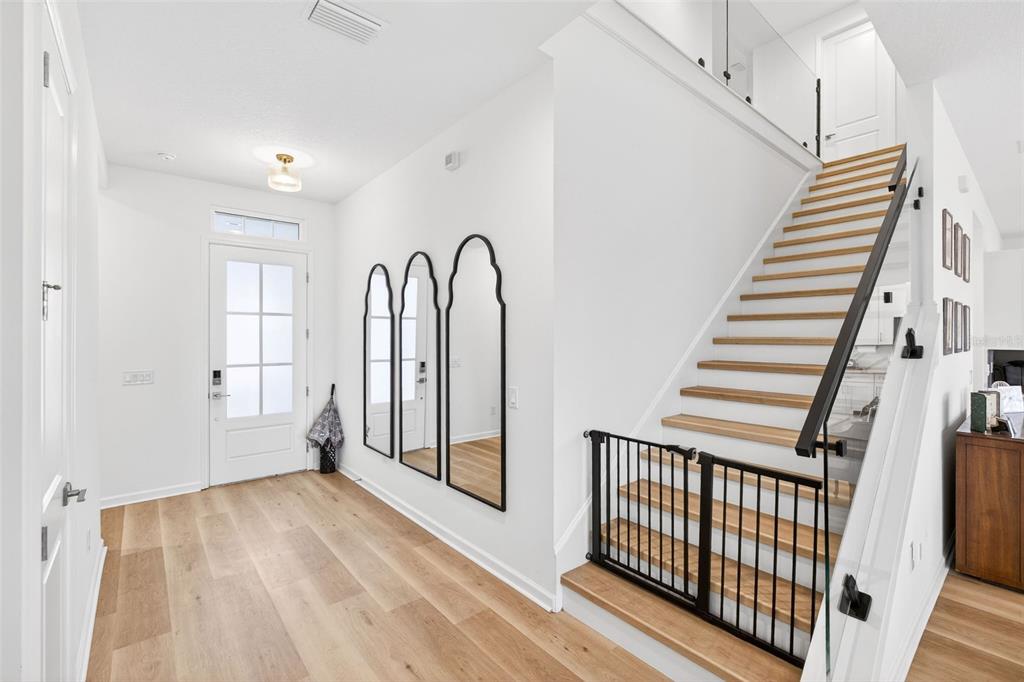 A bright entryway features light wood flooring, a staircase with a black gate, and arched mirrors — 6604 QUEST STREET, ST CLOUD, FL