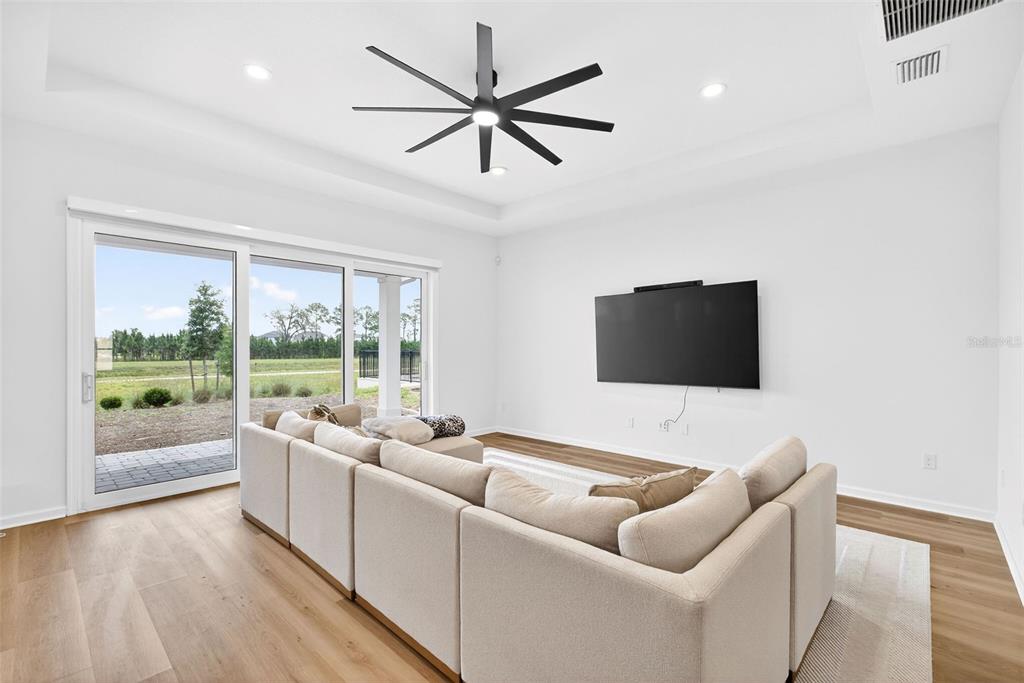 A living room features a large sectional sofa, a wall-mounted television, and sliding glass doors — 6604 QUEST STREET, ST CLOUD, FL
