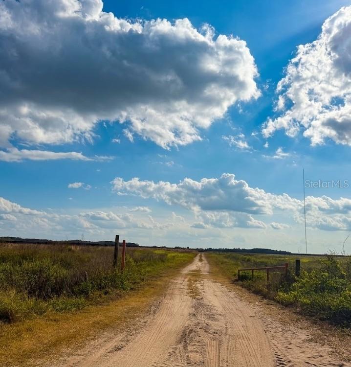 A dirt path leads through an open, grassy field under a bright, cloudy blue sky — HOLOPAW GROVES ROAD LOT 22, ST CLOUD, FL