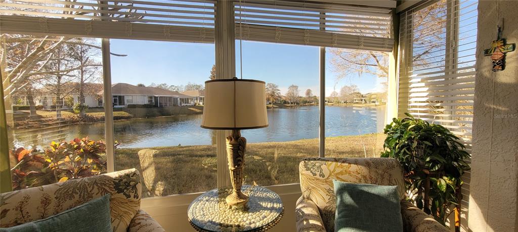 A sunroom with a lamp on a small table overlooks a lake and houses — 834 TREMONT GREENS LANE UNIT 137, SUN CITY CENTER, FL