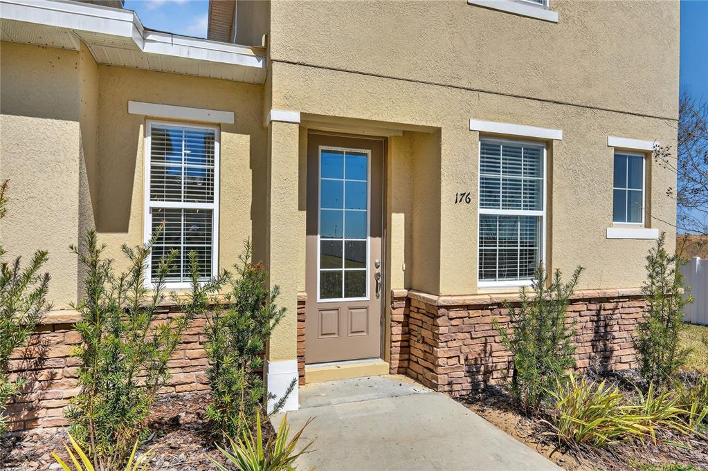 The exterior of a tan stucco house features a brown front door and stone siding — 176 HOLLY VILLAGE DRIVE, DAVENPORT, FL
