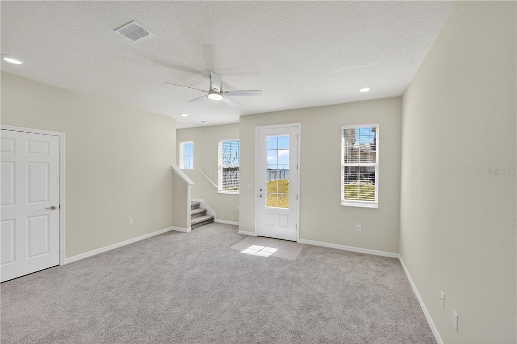 A carpeted room features a ceiling fan, a white door, and stairs leading upward — 176 HOLLY VILLAGE DRIVE, DAVENPORT, FL