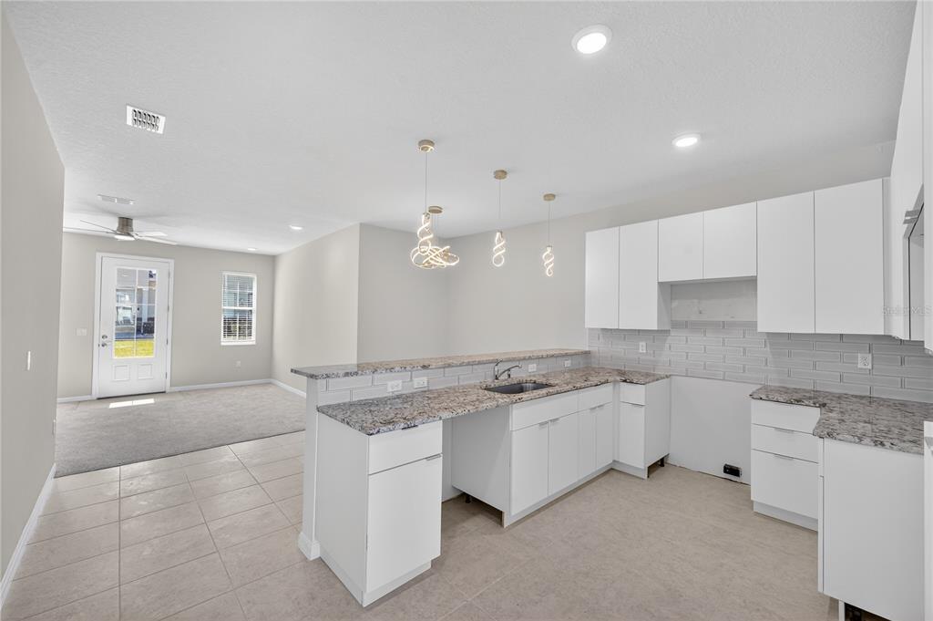 A kitchen with white cabinets, granite countertops, and a tile backsplash opens to a living area — 176 HOLLY VILLAGE DRIVE, DAVENPORT, FL