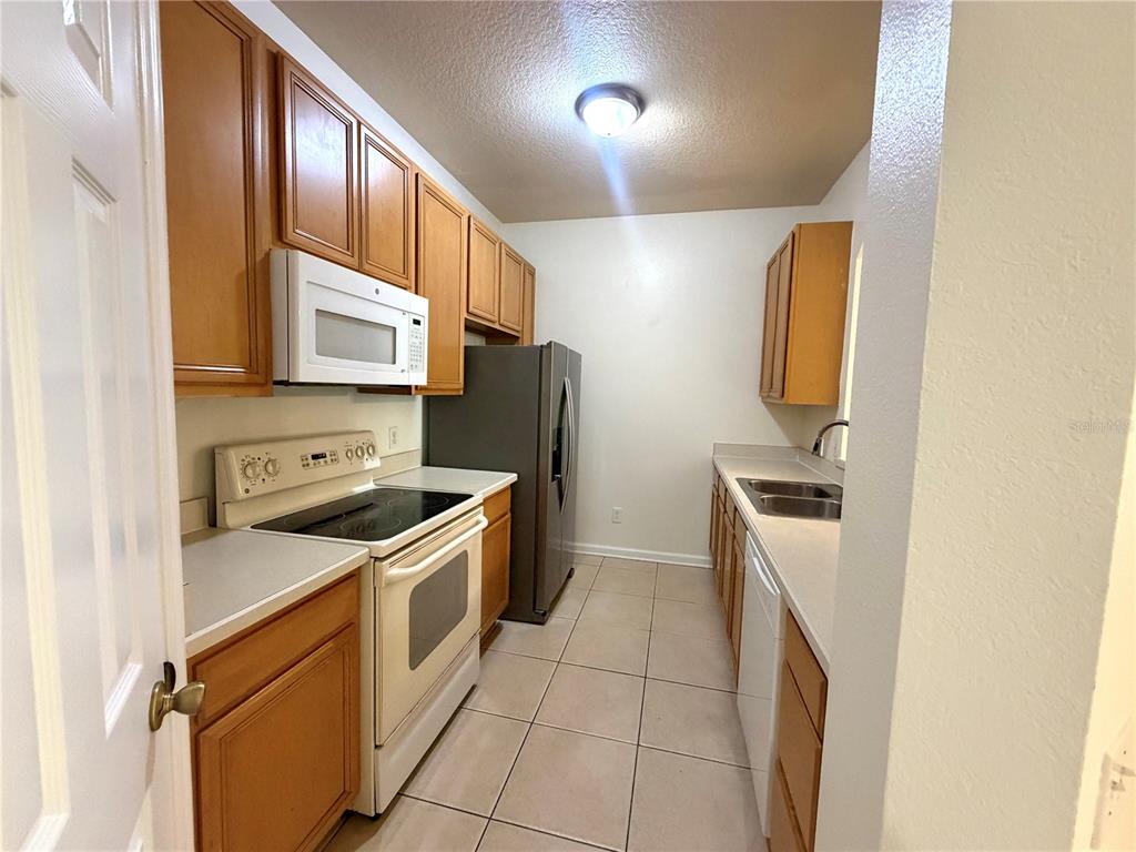 A galley kitchen features wood cabinets, white appliances, a stainless steel refrigerator, and tile flooring — 6084 STEVENSON DRIVE UNIT 204, ORLANDO, FL