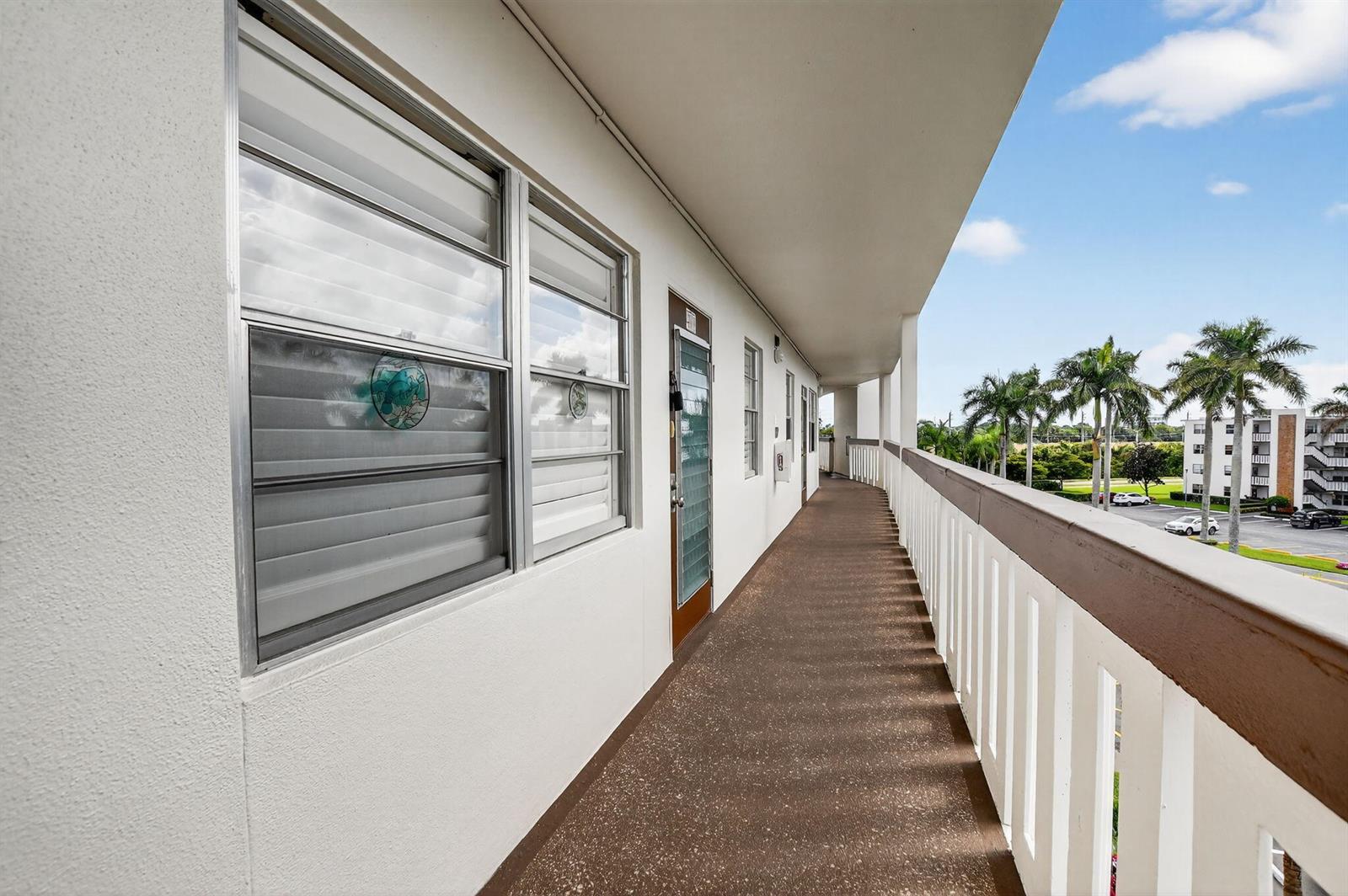 An outdoor apartment walkway with white walls, brown flooring, and a white railing — 4008 Hythe A, Boca Raton FL 33434, BOCA RATON, FL