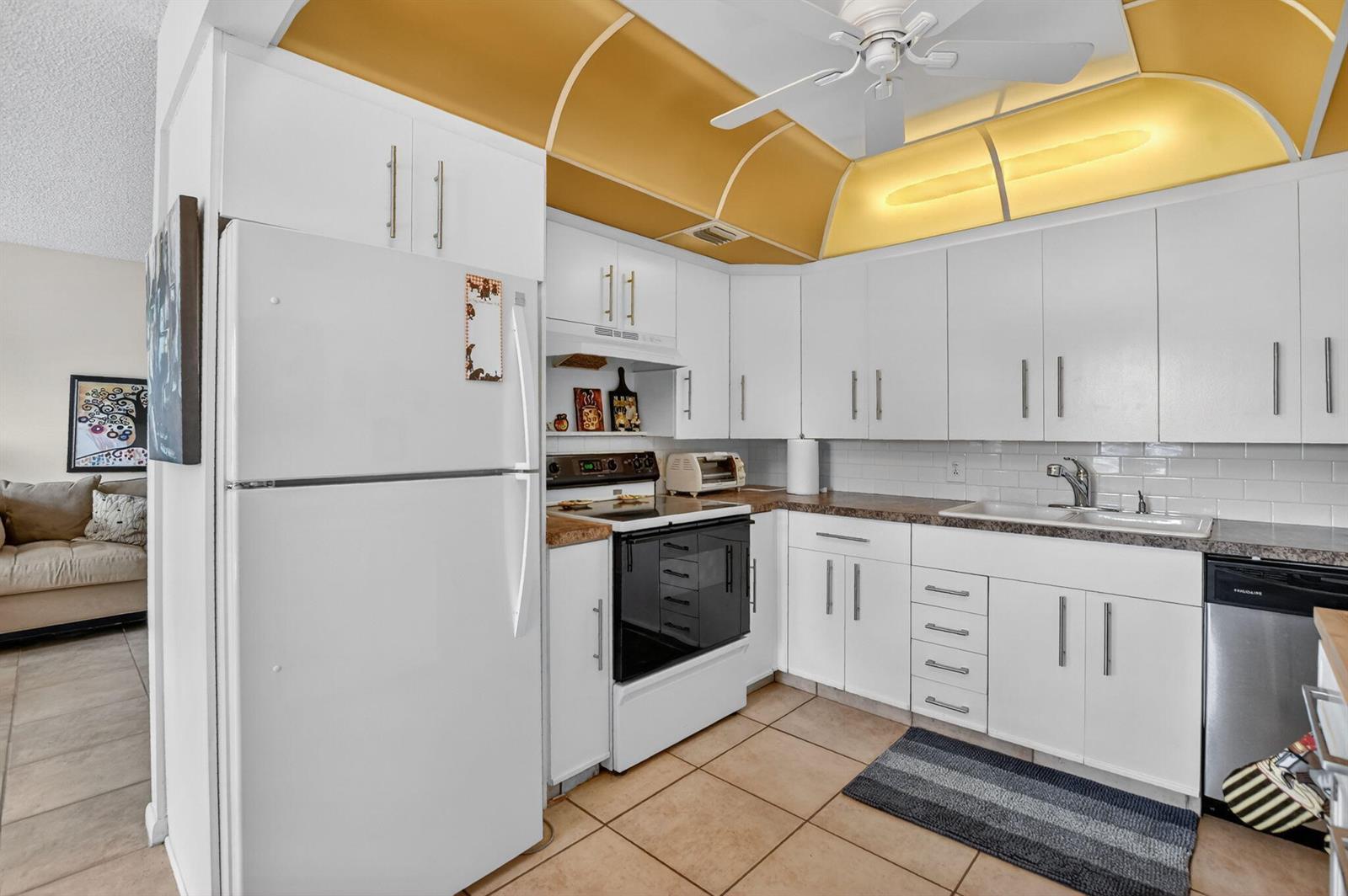 A kitchen features white cabinets, a black stove, a white refrigerator, and a gold soffit — 4008 Hythe A, Boca Raton FL 33434, BOCA RATON, FL