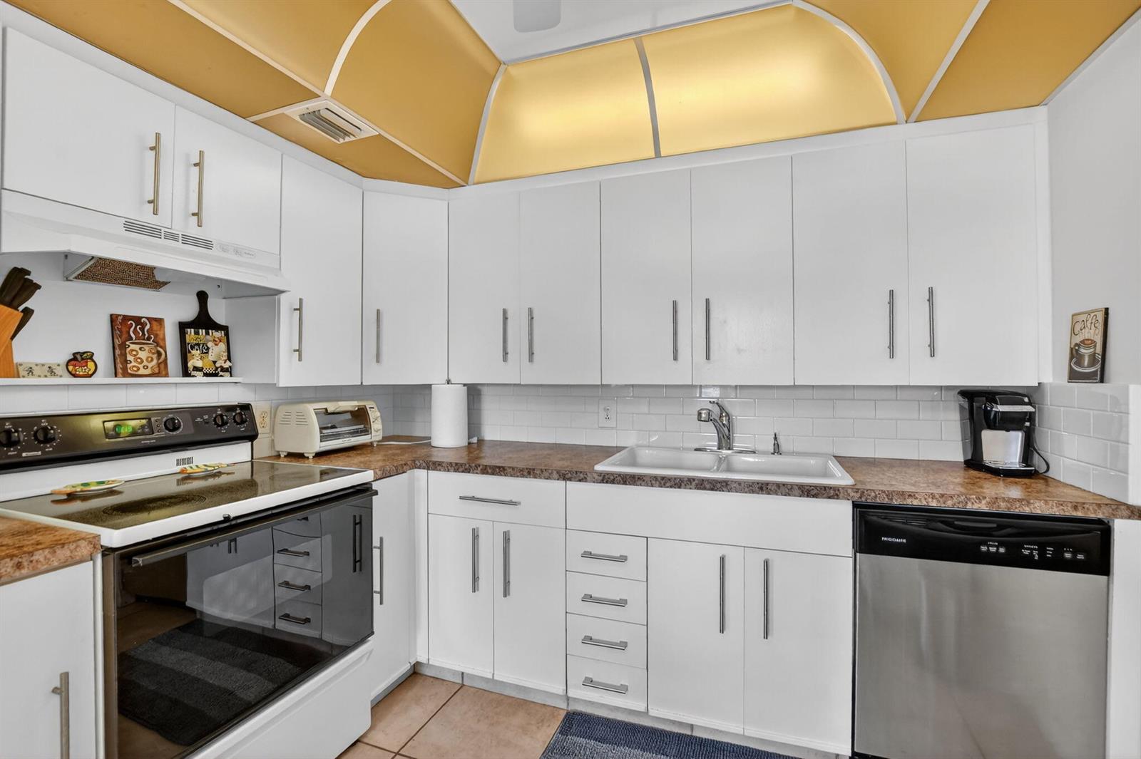 A kitchen with white cabinets, a brown countertop, a stainless steel dishwasher, and yellow lighting — 4008 Hythe A, Boca Raton FL 33434, BOCA RATON, FL