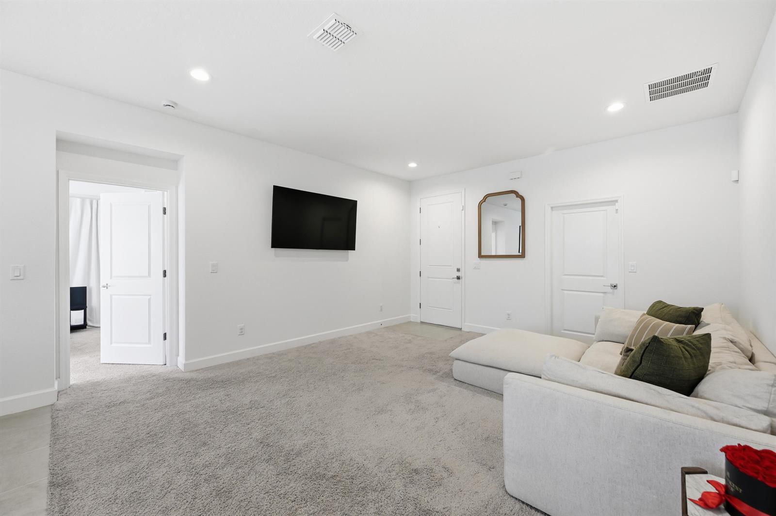 A living room features white walls, gray carpeting, a wall-mounted television, and a sectional sofa — 8452 Dorsey Street, Spring Hill FL 34608, SPRING HILL, FL