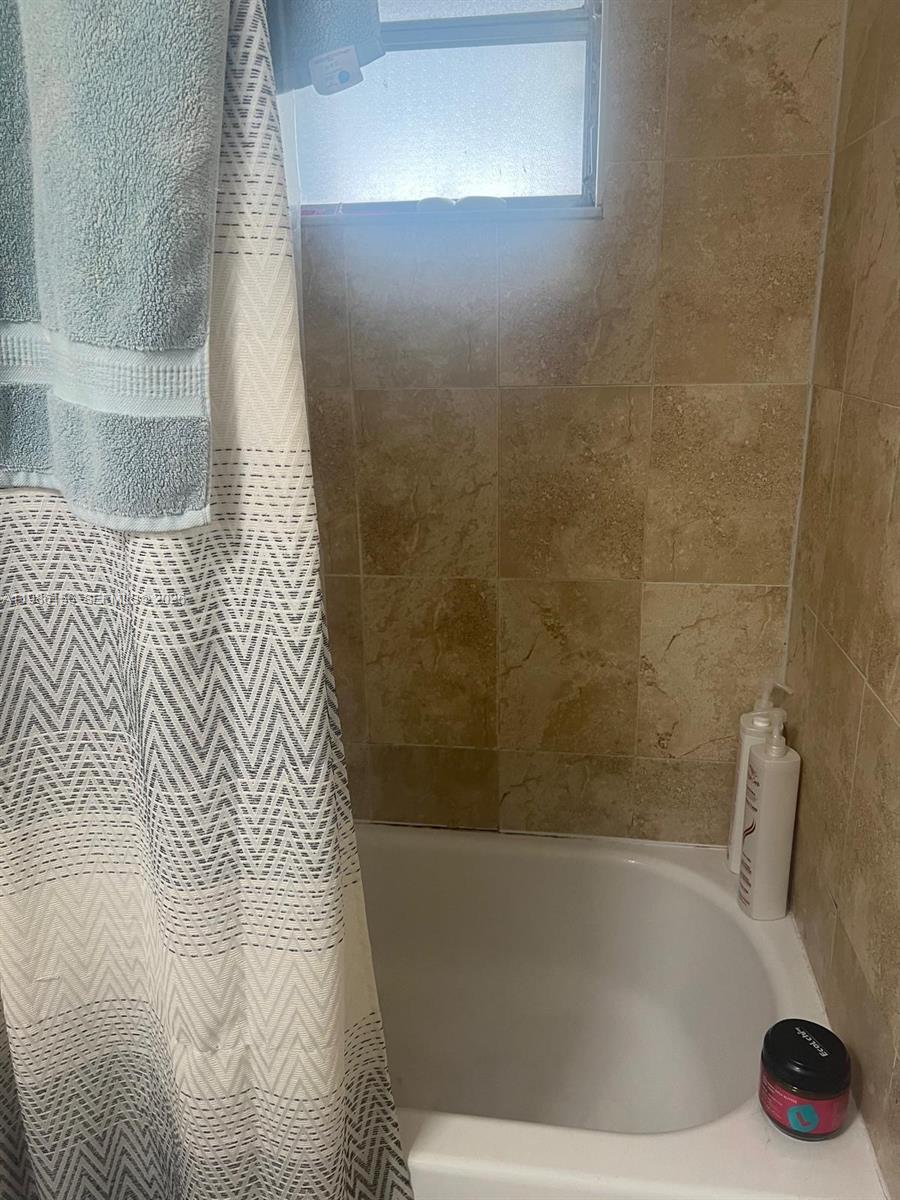 A bathroom features a white bathtub, tan tiled walls, and a patterned shower curtain — 3901 SW 112th Ave # 34, Miami FL 33165, MIAMI, FL