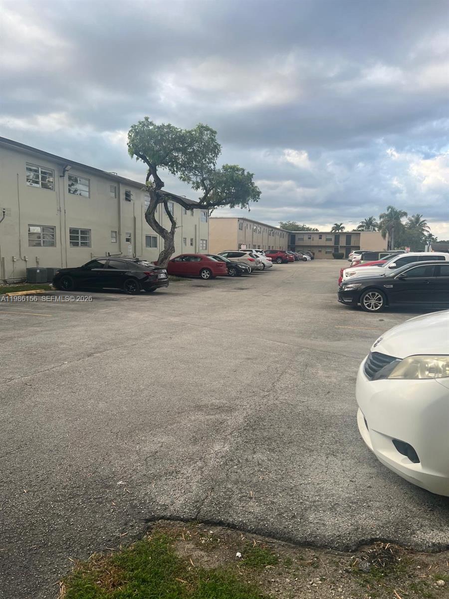 An outdoor parking lot is situated between two multi-story apartment buildings under a cloudy sky — 3901 SW 112th Ave # 34, Miami FL 33165, MIAMI, FL