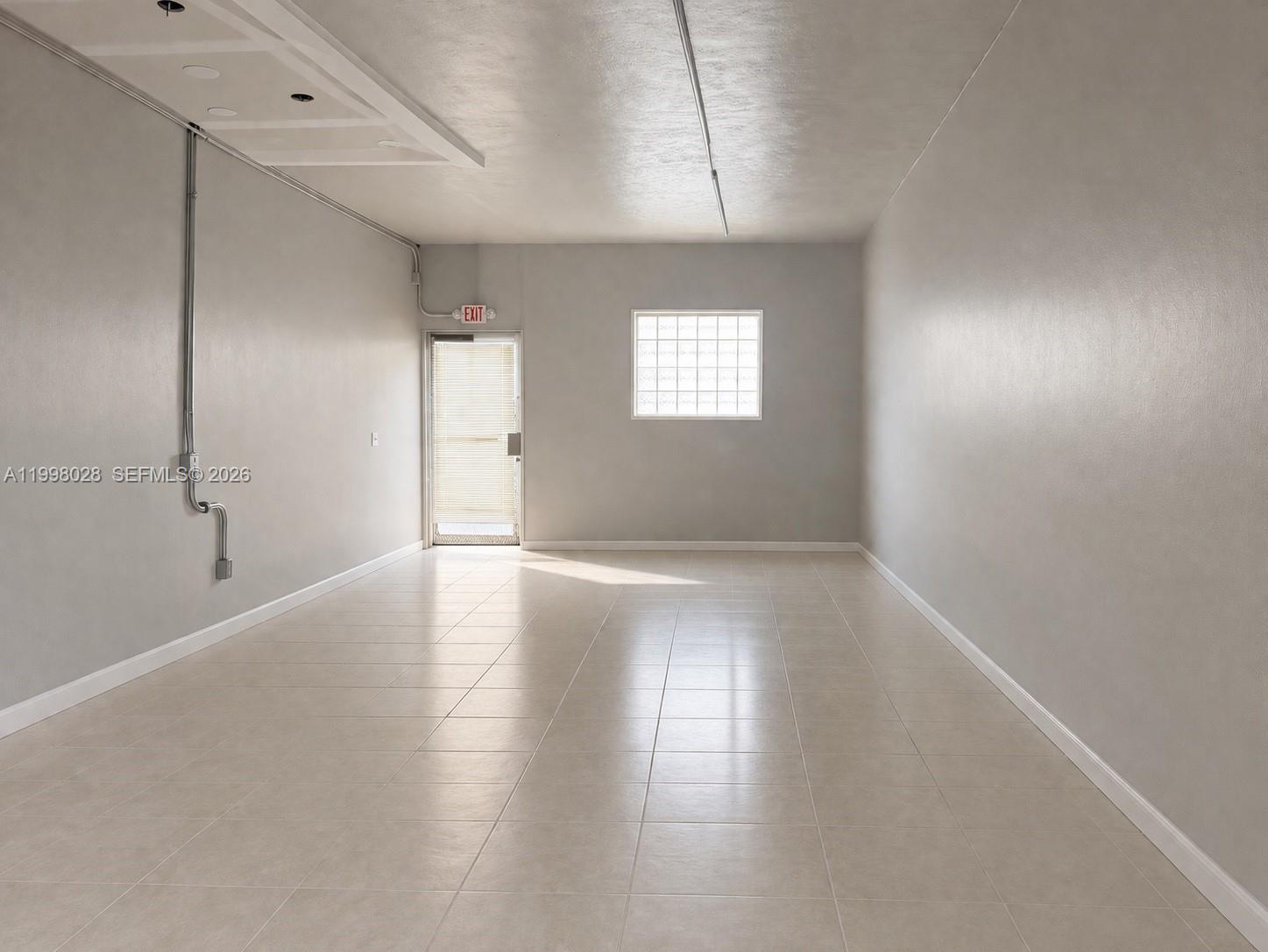 An empty room features light-colored tile flooring, gray walls, a glass block window, and an exit — 7509 NW 22nd Ave, Miami FL 33147, MIAMI, FL