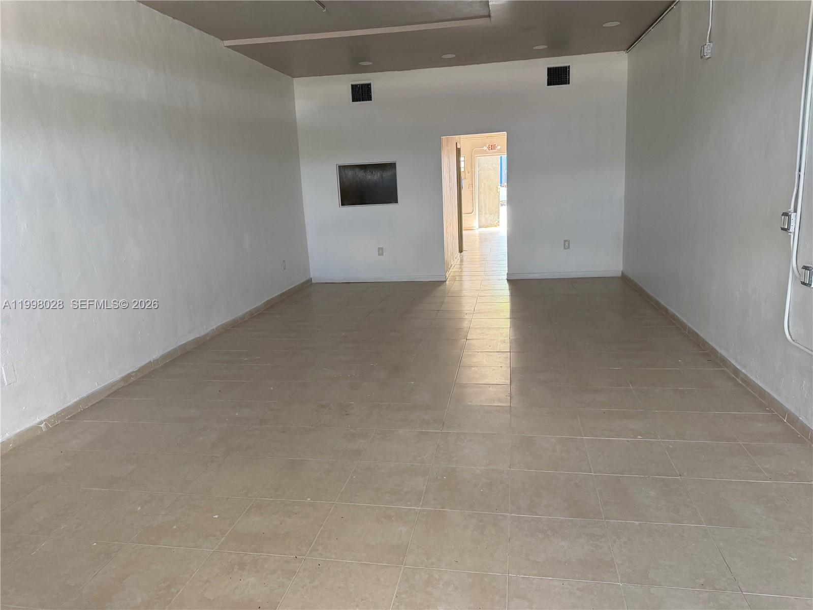 An empty commercial space features white walls, beige tile flooring, and a rear exit door — 7509 NW 22nd Ave, Miami FL 33147, MIAMI, FL
