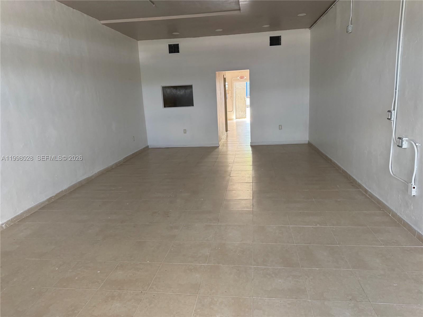 An empty commercial space features white walls, beige tile flooring, and a rear doorway — 7509 NW 22nd Ave, Miami FL 33147, MIAMI, FL