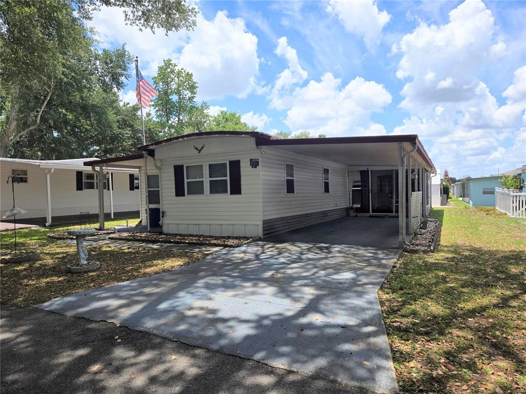 A single-story manufactured home with a carport and an American flag in the front yard — 6235 PARKSEND LANE, ZEPHYRHILLS, FL
