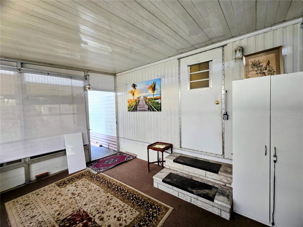 A sunroom features a white door with steps, a patterned rug, and a wall picture — 6235 PARKSEND LANE, ZEPHYRHILLS, FL