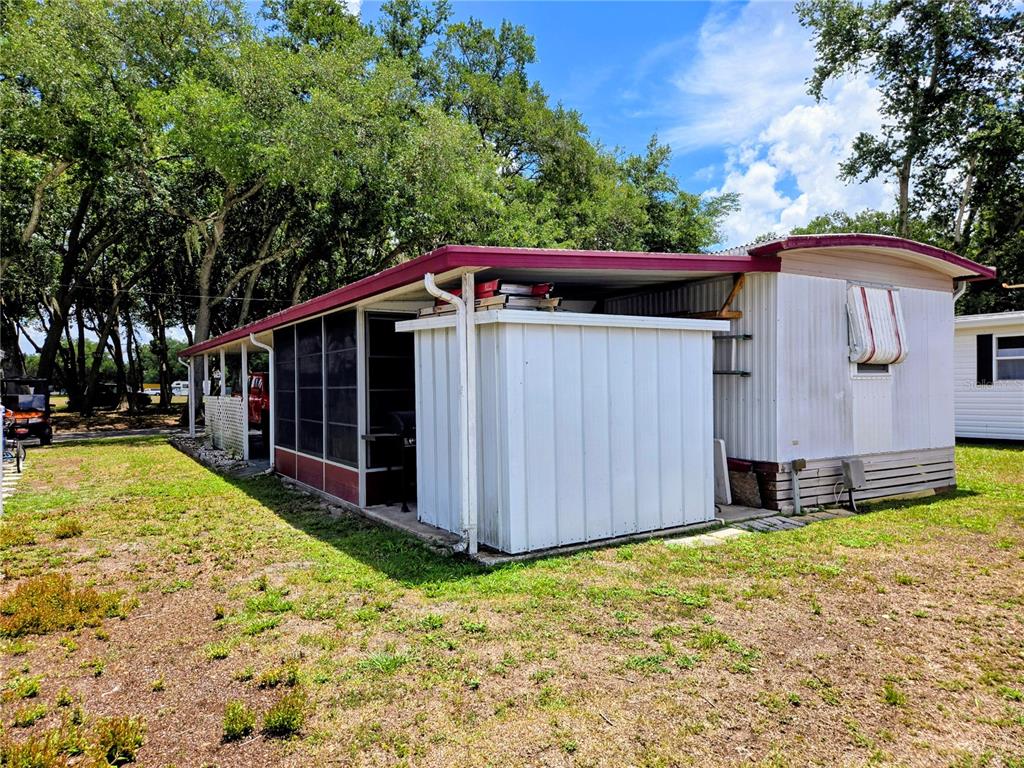 A mobile home exterior features a white storage shed and a screened-in porch area — 6235 PARKSEND LANE, ZEPHYRHILLS, FL