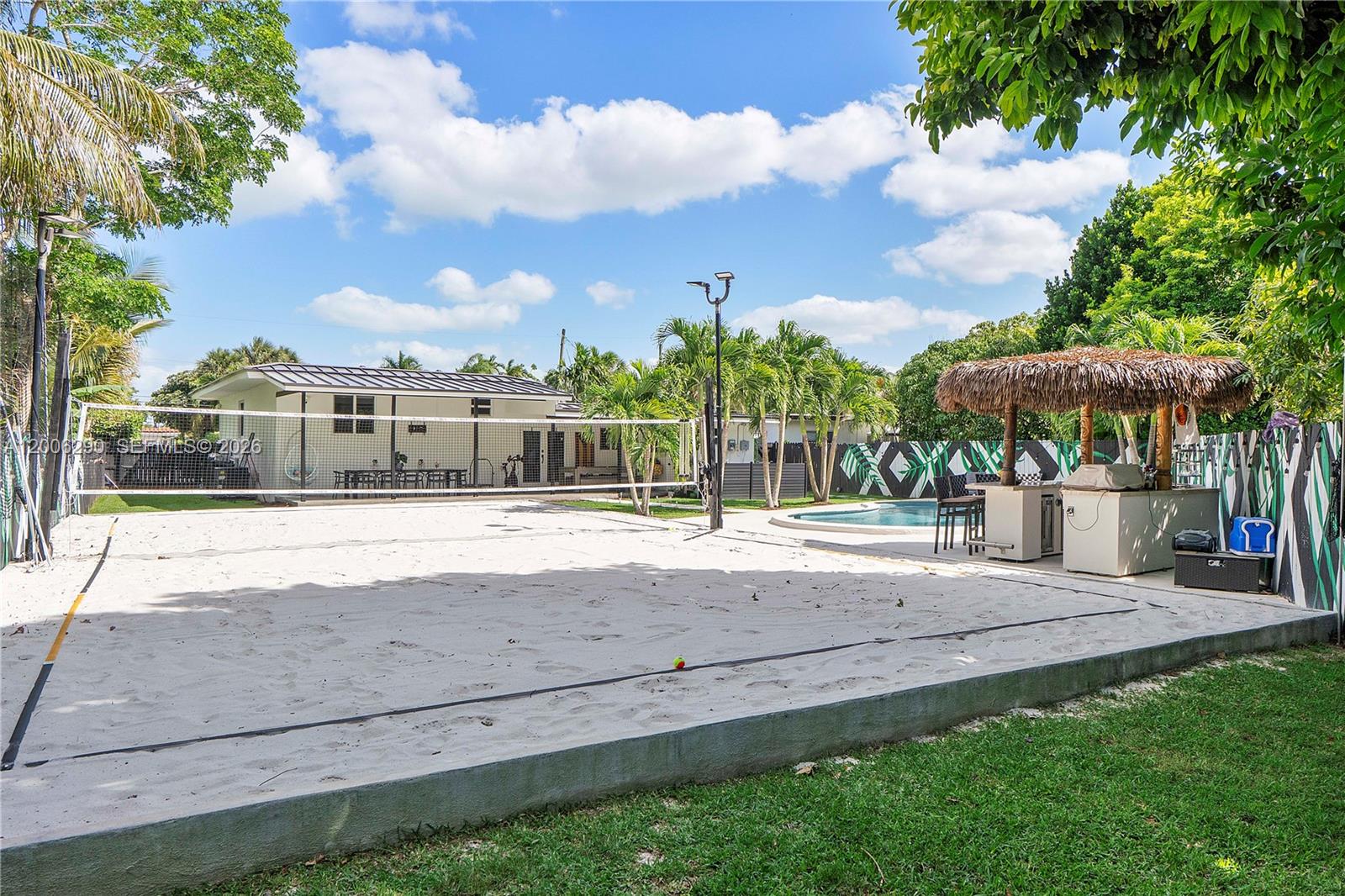 A sand volleyball court sits in a backyard next to a pool and tiki bar — 14830 N Spur Dr, Miami FL 33161, MIAMI, FL