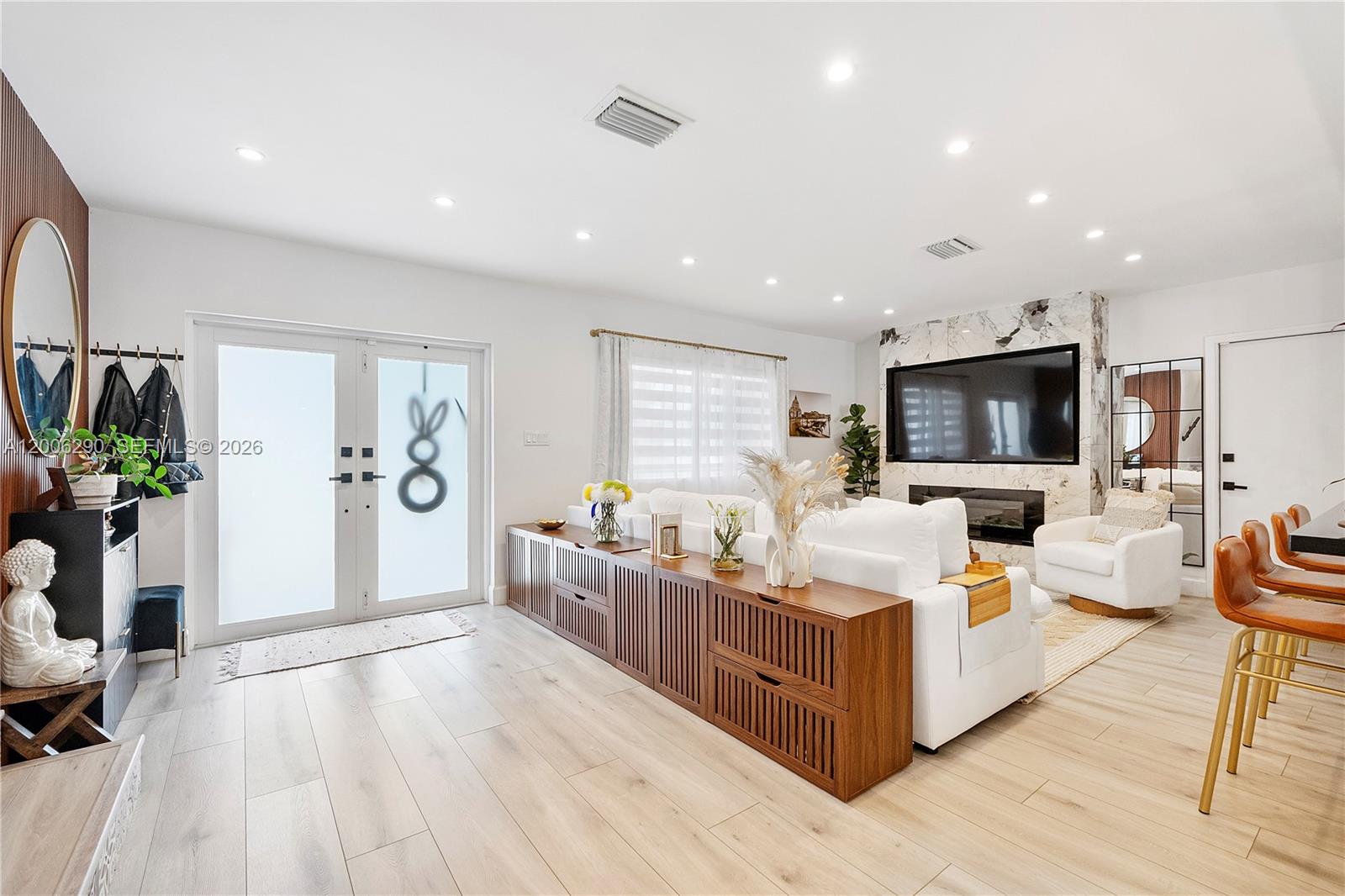 A modern living room features a white sofa, a marble fireplace, and wood-slatted storage consoles — 14830 N Spur Dr, Miami FL 33161, MIAMI, FL