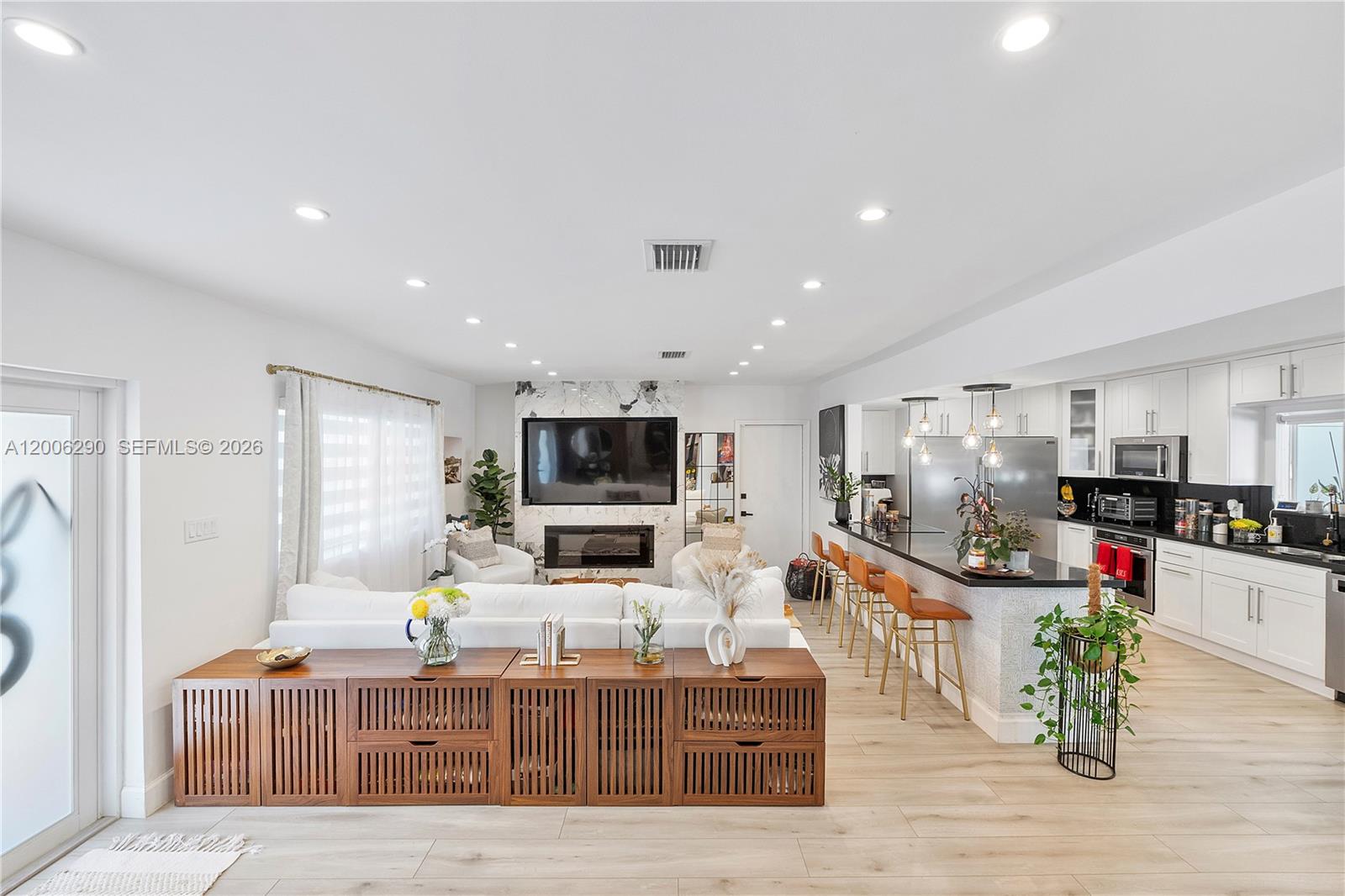 An open-concept living room and kitchen feature white cabinetry, a marble fireplace, and wood flooring — 14830 N Spur Dr, Miami FL 33161, MIAMI, FL