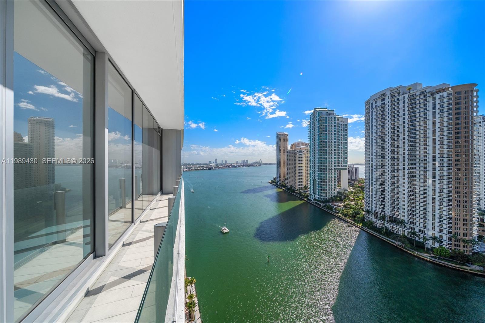A high-rise balcony overlooks a waterway lined with tall residential buildings under a blue sky — 300 Biscayne Blvd Way # 1904C, Miami FL 33131, MIAMI, FL
