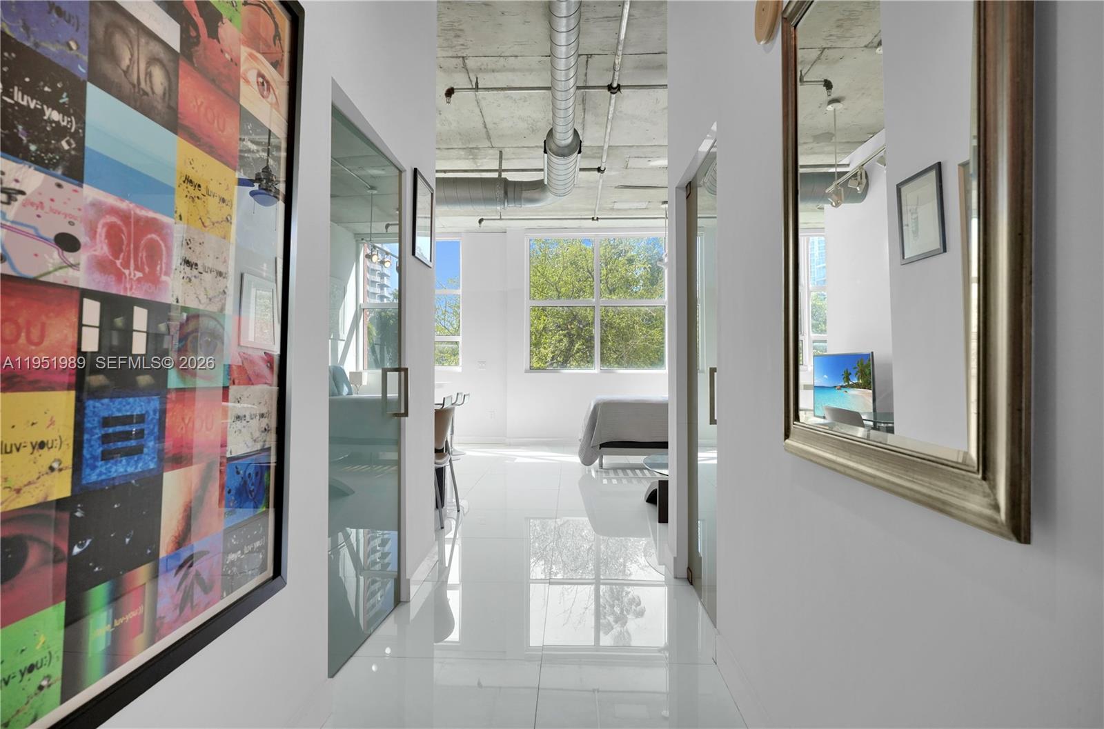 A white hallway with glass doors leads to a bedroom with large windows and concrete ceilings — 2001 Biscayne Blvd # 3213, Miami FL 33137, MIAMI, FL