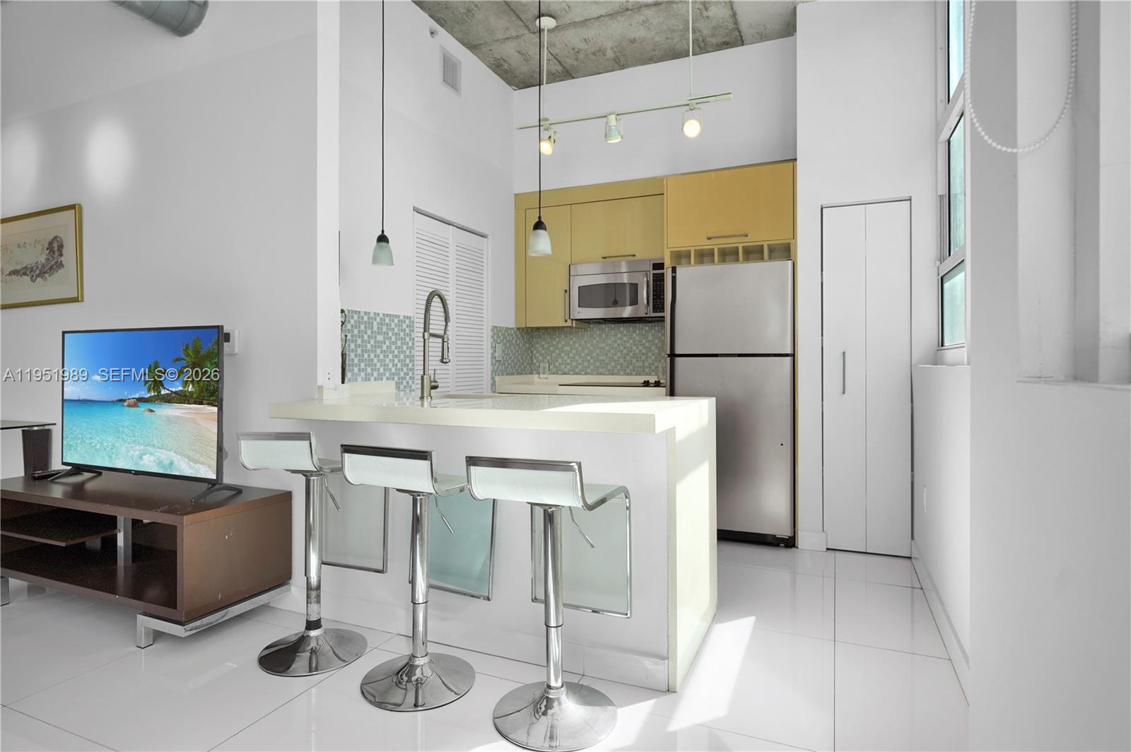 A modern kitchen features a breakfast bar with three stools and light-colored cabinetry — 2001 Biscayne Blvd # 3213, Miami FL 33137, MIAMI, FL