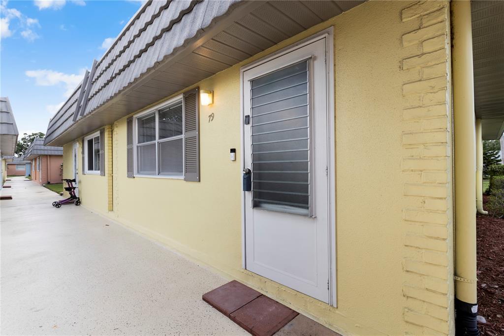 A yellow exterior wall features a white door with a louvered window and a window — 201 BEDFORD STREET UNIT 79, SUN CITY CENTER, FL