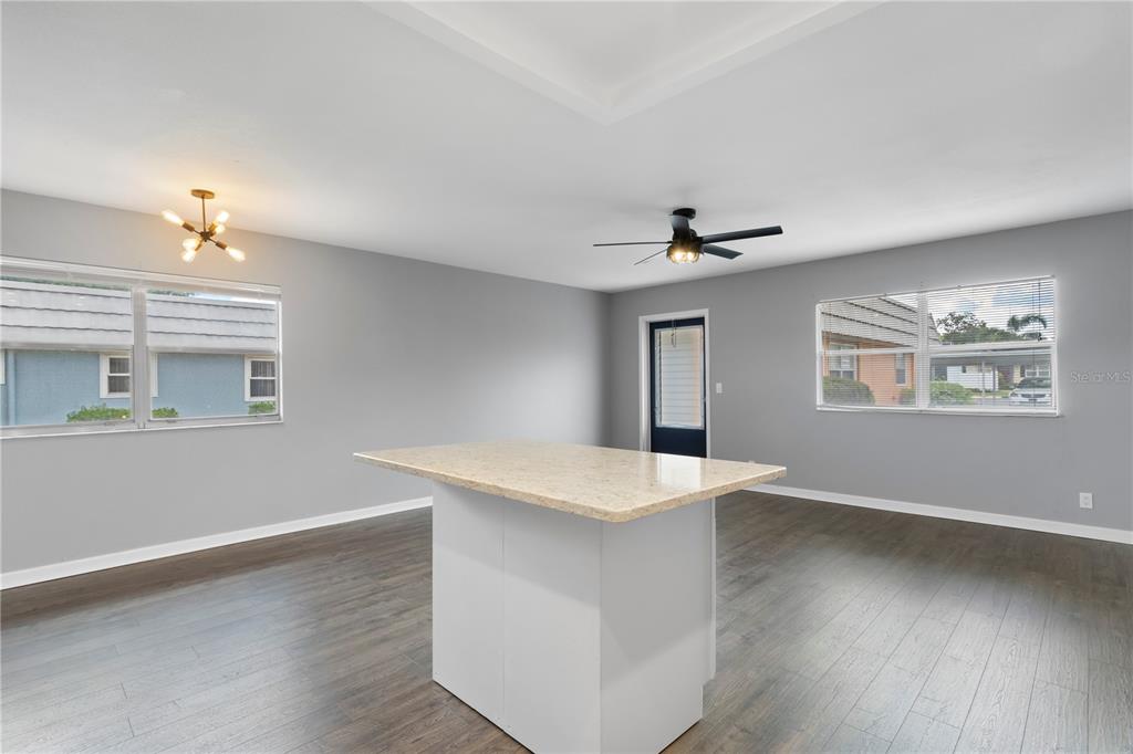 A room with gray walls, dark wood-look flooring, a kitchen island, and two windows — 201 BEDFORD STREET UNIT 79, SUN CITY CENTER, FL