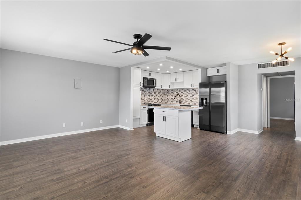 An open-concept kitchen with white cabinets and an island overlooks a spacious living area — 201 BEDFORD STREET UNIT 79, SUN CITY CENTER, FL