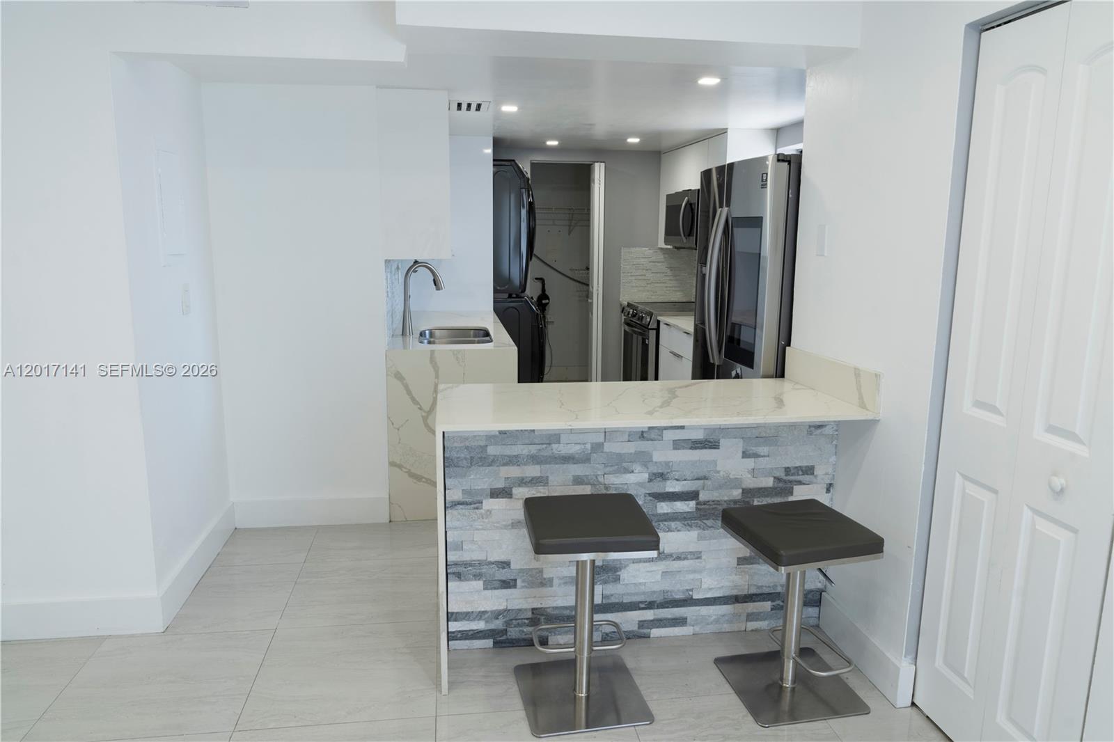 A kitchen features a stone-topped breakfast bar, two stools, and stainless steel appliances — 13850 SW 62nd St # 303, Miami FL 33183, MIAMI, FL