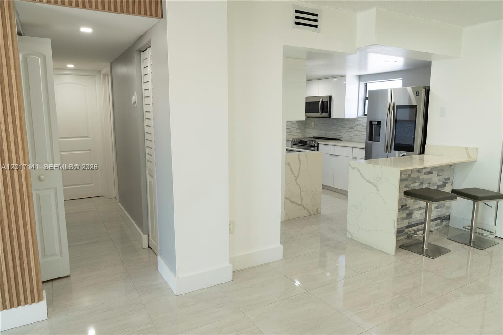 A modern kitchen with white cabinets, stone countertops, and a breakfast bar with two stools — 13850 SW 62nd St # 303, Miami FL 33183, MIAMI, FL