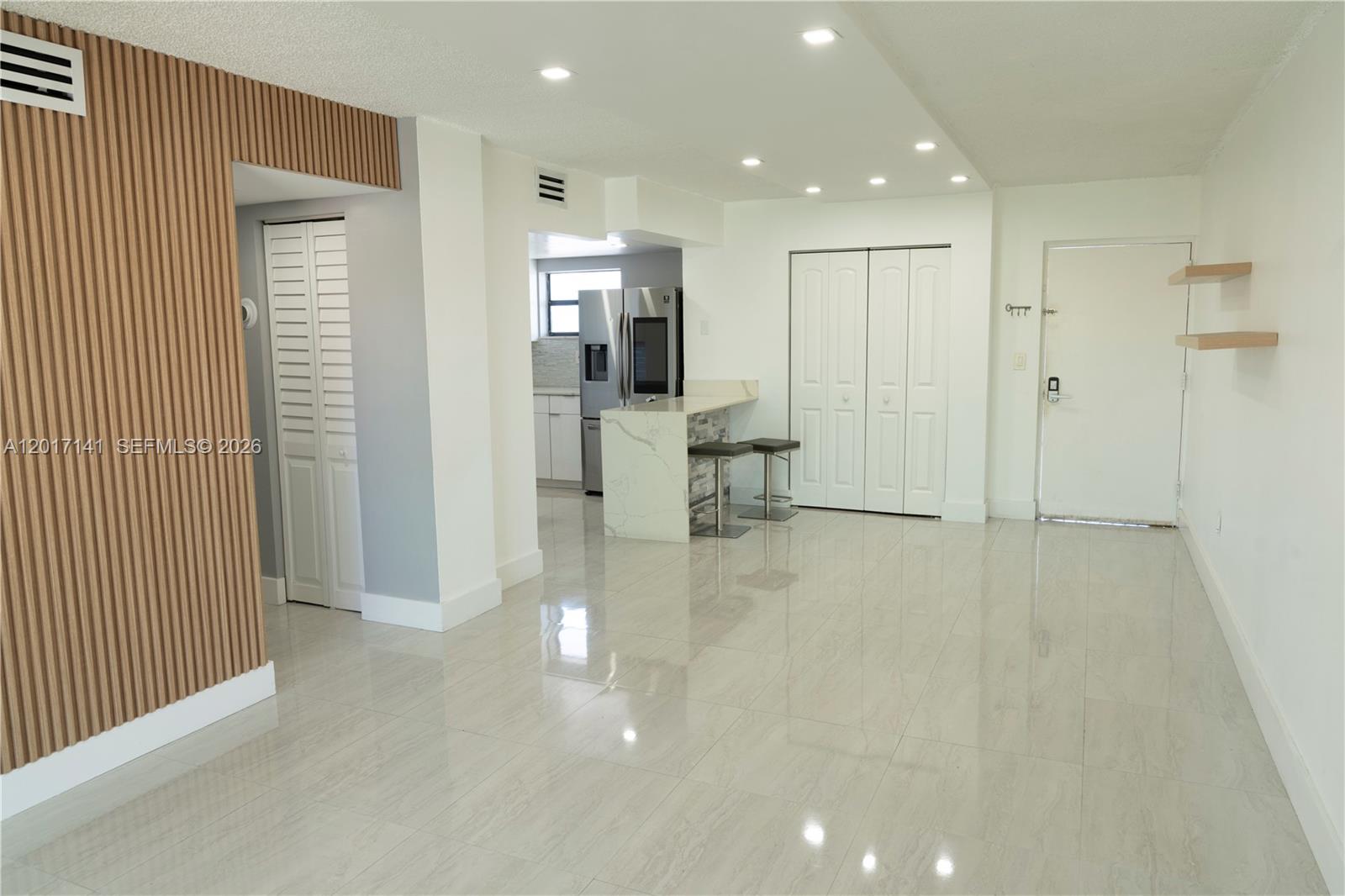 A bright, open-concept living area features light tile flooring, a kitchen island, and wood-slat paneling — 13850 SW 62nd St # 303, Miami FL 33183, MIAMI, FL