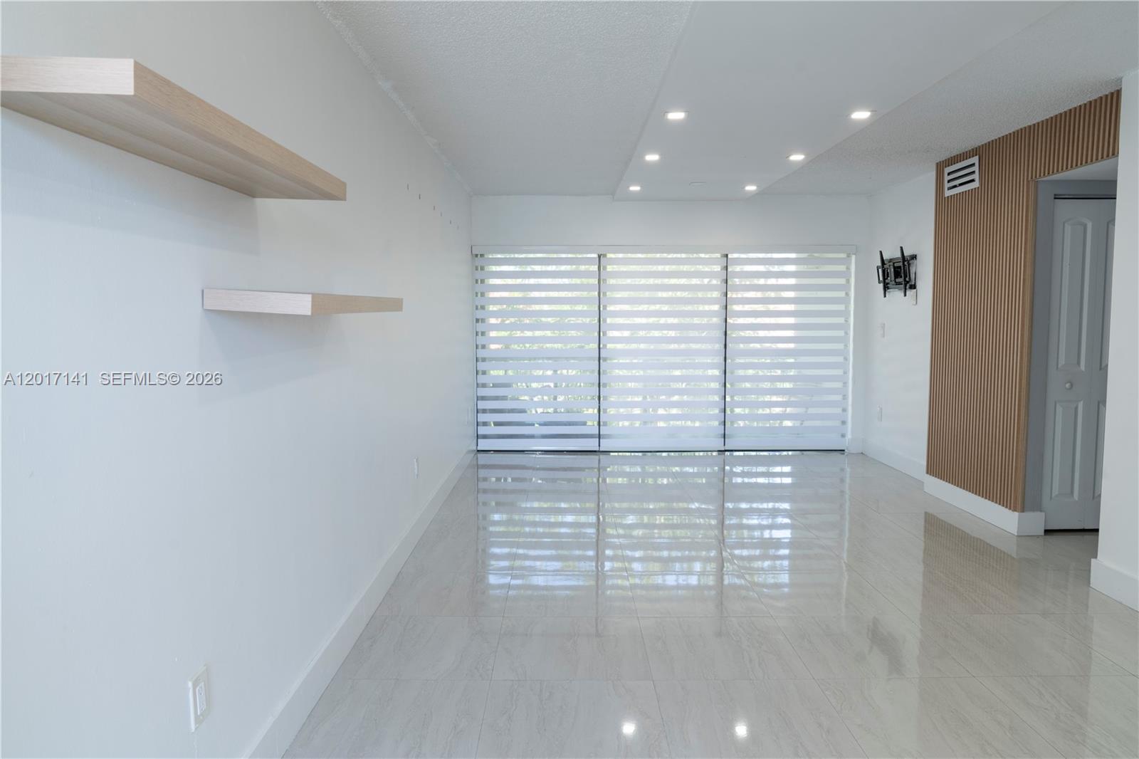 A bright, empty room features light-colored tile flooring, floating shelves, and a slatted wood wall — 13850 SW 62nd St # 303, Miami FL 33183, MIAMI, FL
