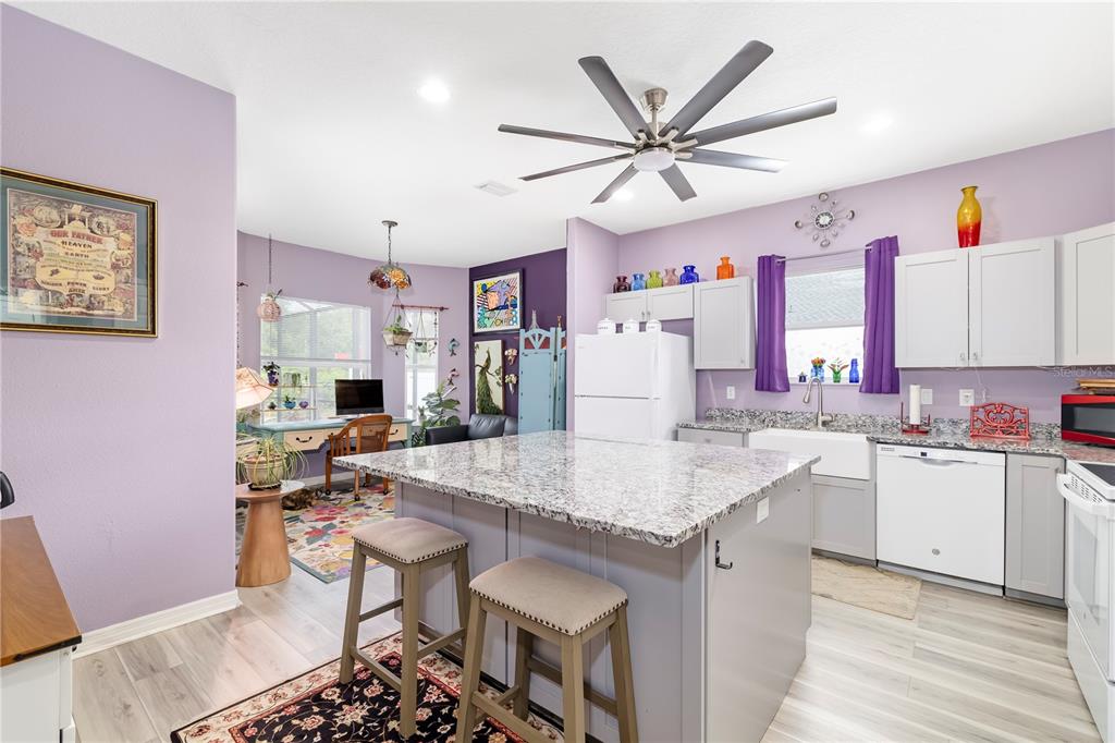 A kitchen with a granite island, gray cabinets, and light purple walls opens to a workspace — 2434 BISMARCK ROAD, NORTH PORT, FL