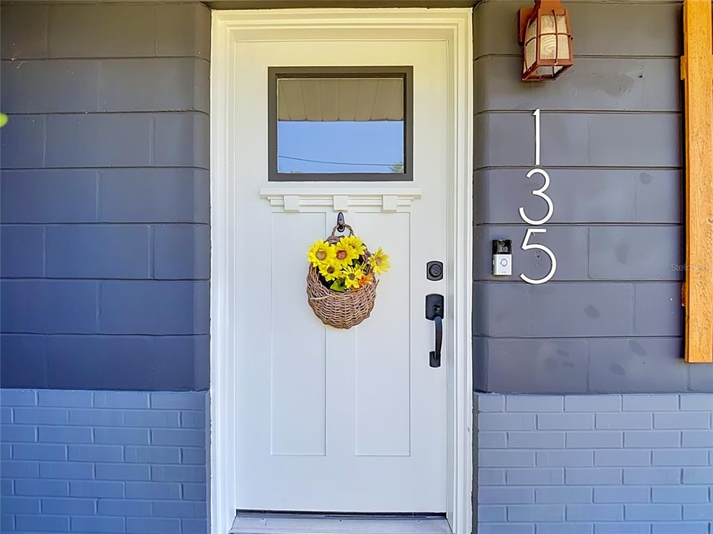 A white front door with a sunflower basket sits between dark gray horizontal and brick siding — 135 CONNIE AVENUE, TAMPA, FL