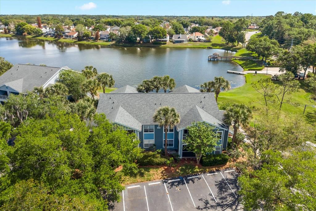 An aerial view shows a multi-story apartment building with a parking lot beside a lake — 2501 GRASSY POINT DRIVE UNIT 103, LAKE MARY, FL