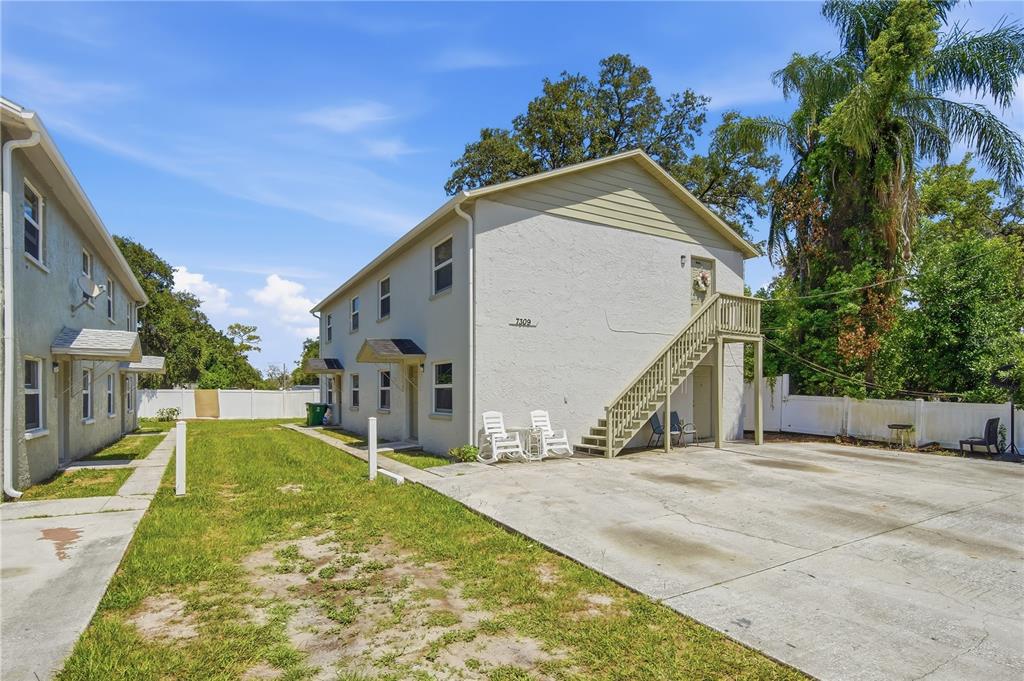 A two-story apartment building features an exterior staircase, concrete driveway, and a grassy yard — 7309 N HUTTON PLACE UNIT D, TAMPA, FL