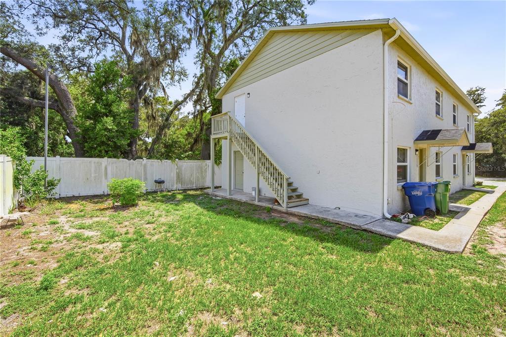 The exterior side of a two-story building features an outdoor wooden staircase and a yard — 7309 N HUTTON PLACE UNIT D, TAMPA, FL