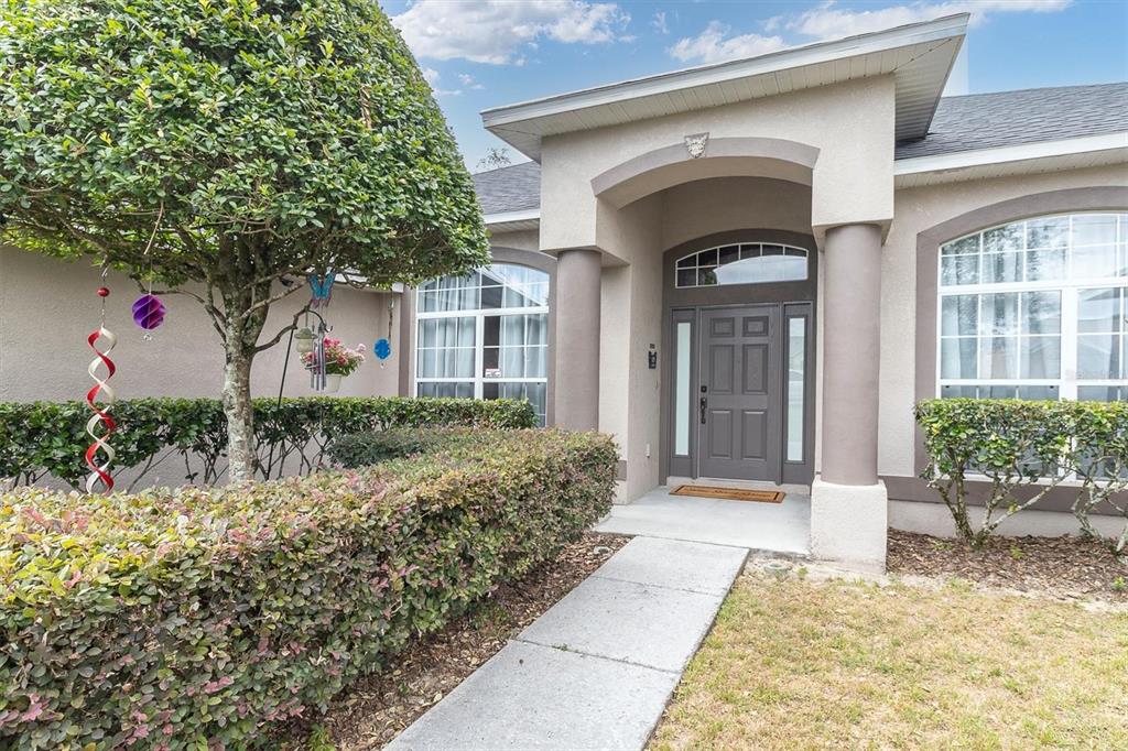 A concrete walkway leads to the front entrance of a house with a gray door — 13270 DRYSDALE STREET, SPRING HILL, FL