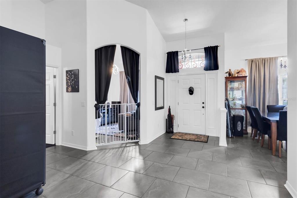 A tiled entryway features a white front door, an arched doorway with curtains, and dining furniture — 13270 DRYSDALE STREET, SPRING HILL, FL