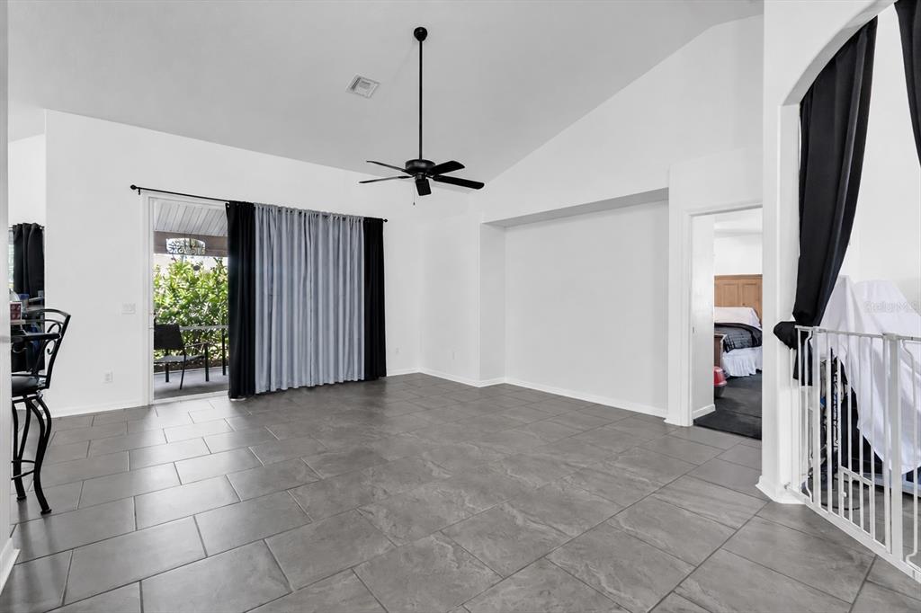 A living room with gray tile flooring, a vaulted ceiling, and a sliding glass door — 13270 DRYSDALE STREET, SPRING HILL, FL