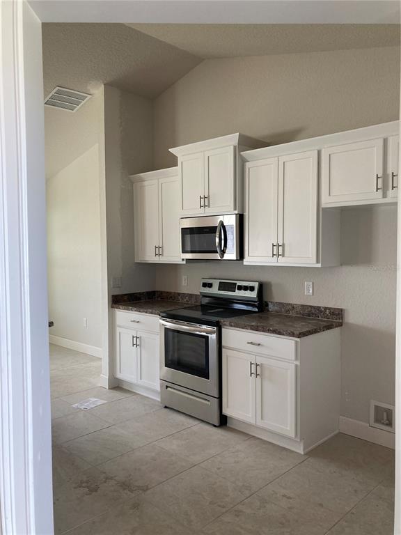 A kitchen features white cabinets, stainless steel appliances, and brown countertops with tile flooring — 8 DOGWOOD PLACE, OCALA, FL
