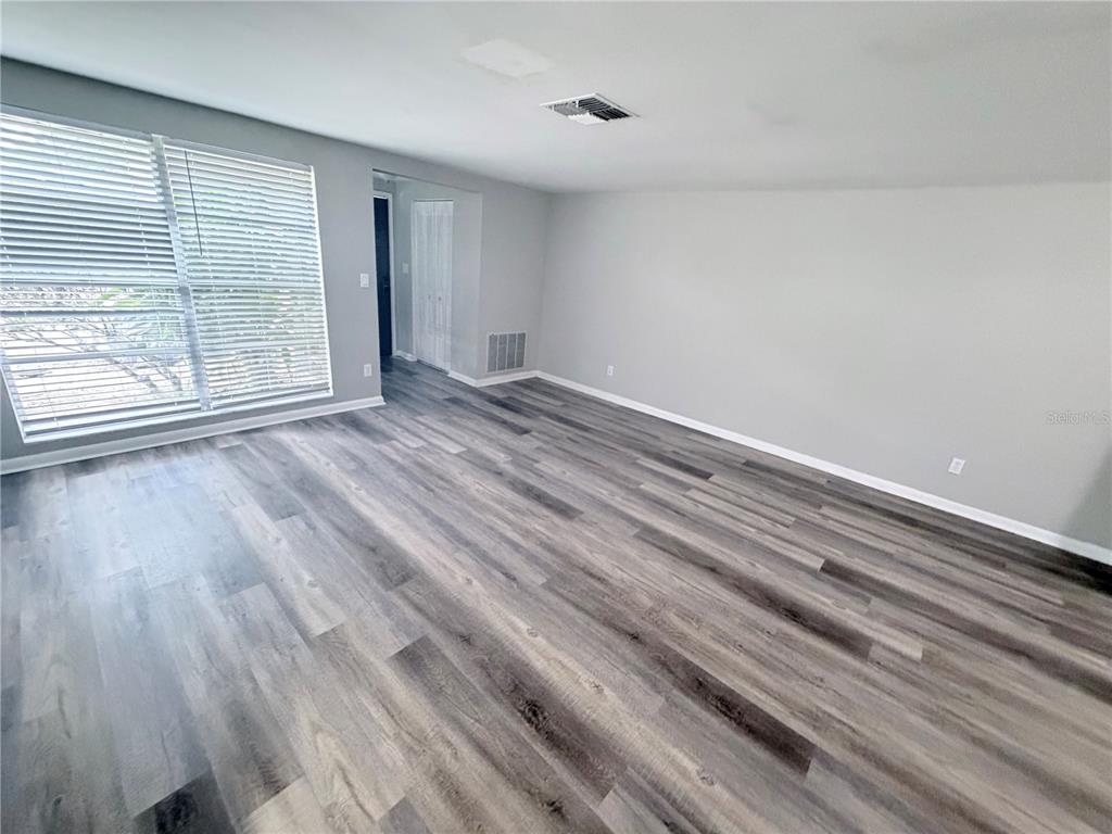An empty room features gray walls, wood-look flooring, a large window with blinds, and recessed lighting — 8923 CANDLEWICK LANE, PORT RICHEY, FL