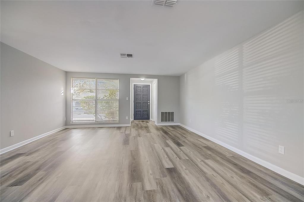 An empty living room features light gray walls, wood-look flooring, and a dark front door — 8923 CANDLEWICK LANE, PORT RICHEY, FL