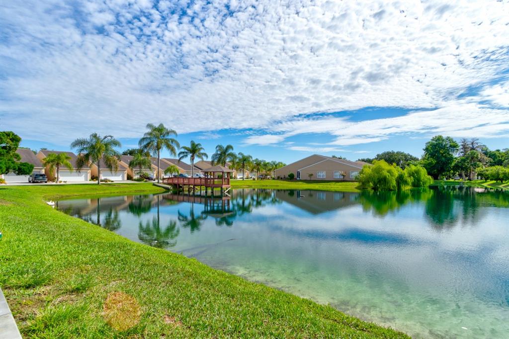 A pond with a wooden gazebo sits in front of residential buildings under a cloudy sky — 2246 HAWKS COVE CIRCLE, NEW SMYRNA BEACH, FL